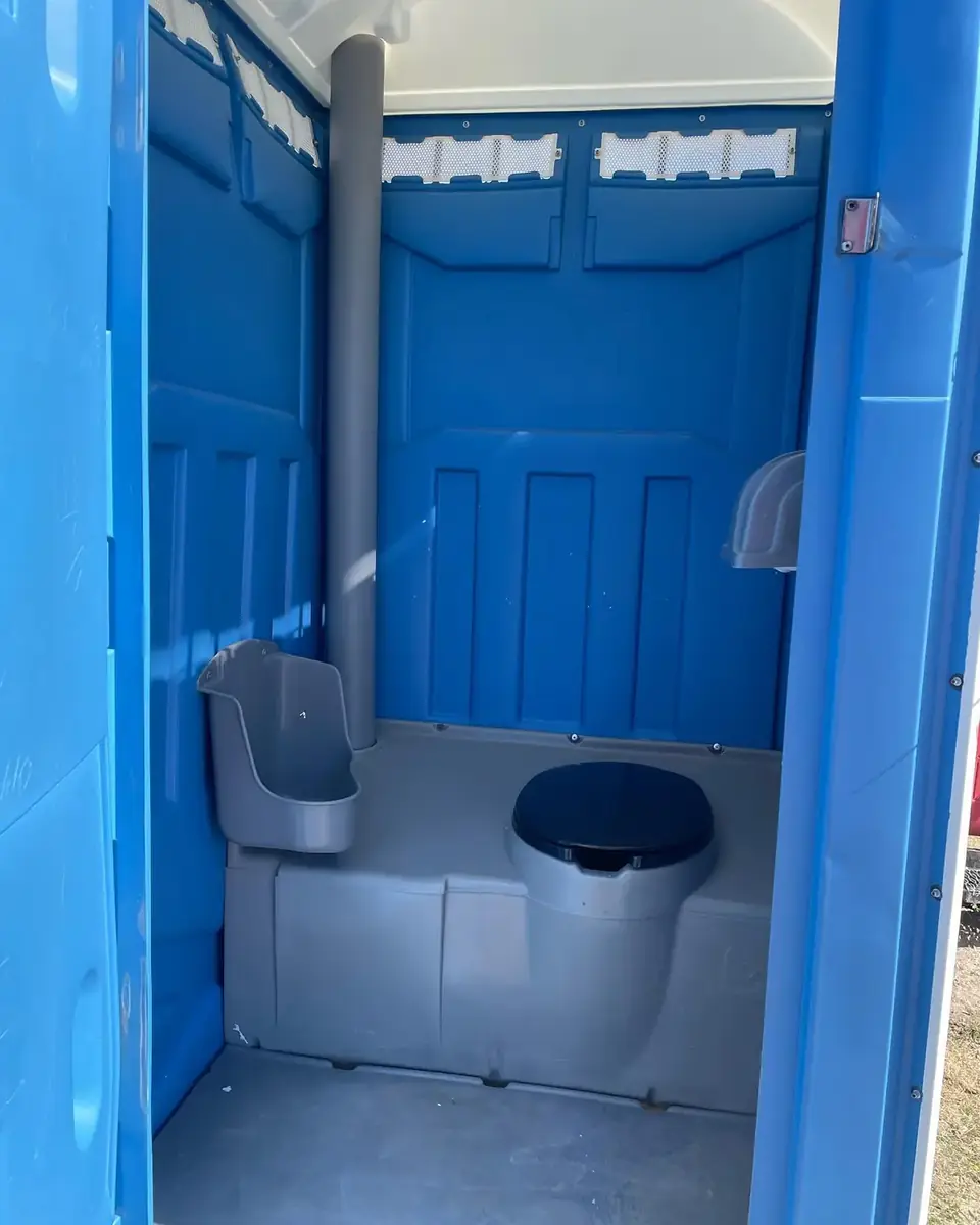 Inside a blue standard porta potty showing the toilet seat and urinal
